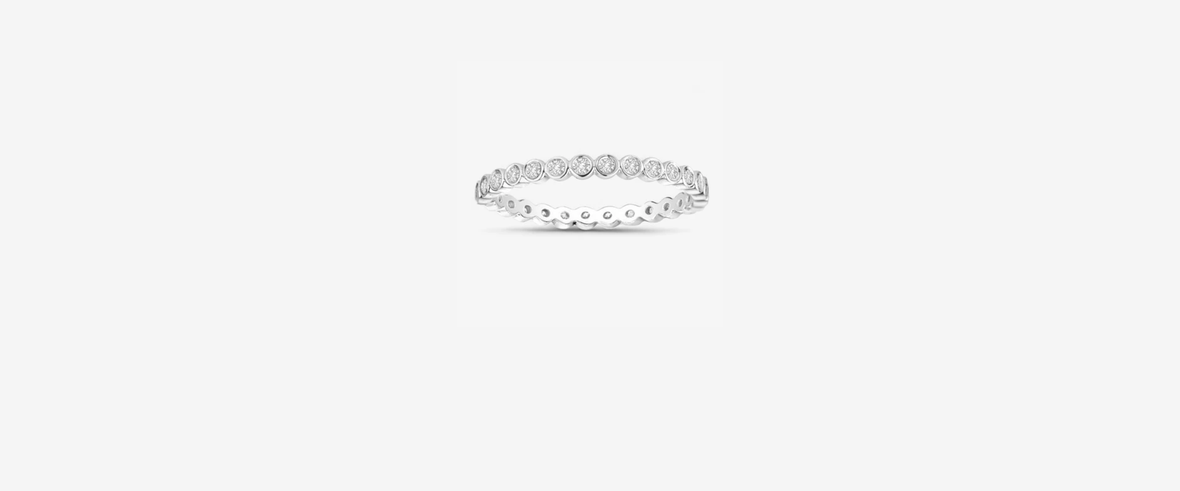 White gold diamond eternity band ring with bezel-set round diamonds encircling the band, scalloped edge detail, light gray background.